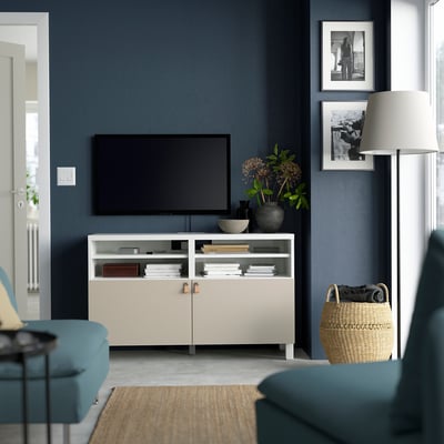 Modern living room with BESTÅ tv bench, flat-screen, flowers, pictures, basket, lamp. Wall is dark blue.