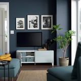 Modern living room with tv on BESTÅ unit, teal couch, yellow blanket, wall art.