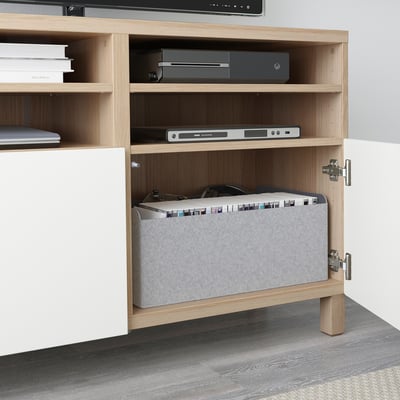 A wooden tv stand with open shelves, housing electronics and a laptop.