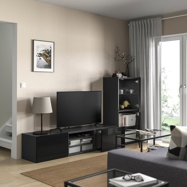 Modern living room with BESTÅ black tv bench, flat screen tv, gray lamp, bookshelf with items, and large window with curtains.