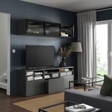 Modern living room with black BESTÅ tv bench, wall cabinets, and drawer unit. Flat-screen tv, decorative items, and a beige curtain.