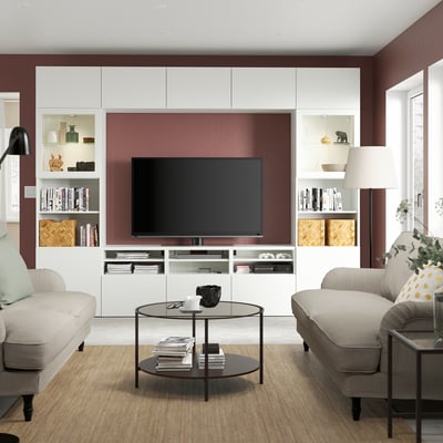 Modern living room with BESTÅ tv unit, shelves, cable outlets, and drawers. Neutral sofas, coffee table, lamp, and plants.