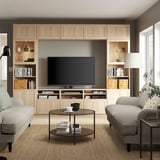 Modern living room with large built-in beige BESTÅ tv unit, two light grey sofas, wooden coffee table, black floor lamp, and potted plant.