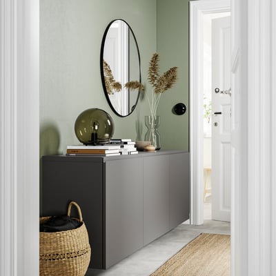 Modern entryway with green walls, grey BESTÅ cabinet, oval mirror, dried plants, lamp, and basket.