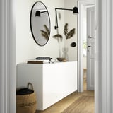 White BESTÅ cabinet with mirror, lamps, basket, doorway.
