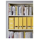 A white bookshelf with three shelves, storing colorful cookbooks and yellow storage boxes, ideal for organizing and displaying books.