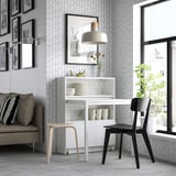 Modern room with BILLY white bookcase desk, black chair, gray sofa, and geometric wallpaper. Large window, black pendant lamp, and framed photos.