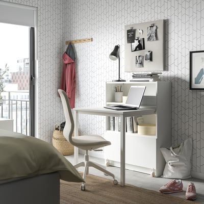 Home office with desk, laptop, chair, lamp, and clothes.