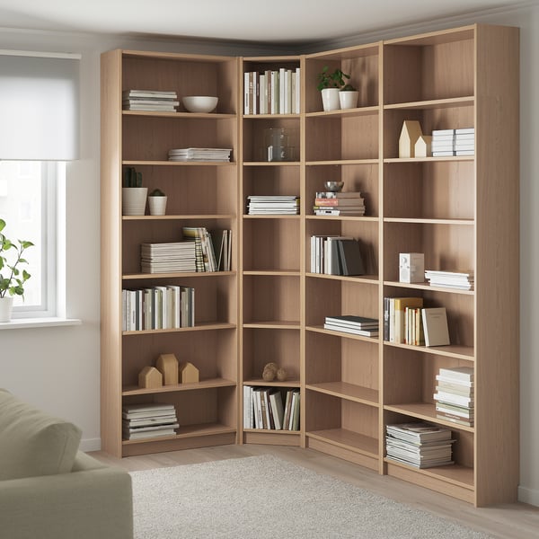 Corner BILLY bookcase in light oak, reaching ceiling with books and decor.