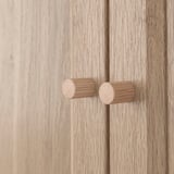 Wooden cabinet with two cylindrical knobs; smooth finish, natural texture.