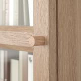 Close-up of wooden bookcase edge, showing smooth, light-brown finish and round, knurled handle.