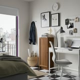 Modern bedroom with BILLY bookcase, laptop, round clock, white chair, green bed blanket, and artworks.