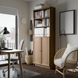 BILLY bookcase in light wood beside desk, chair, near balcony. Books & decor, fits modern minimalist room.