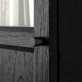 Cylindrical black metal handle on dark wooden door, showcasing natural grain and smooth finish.