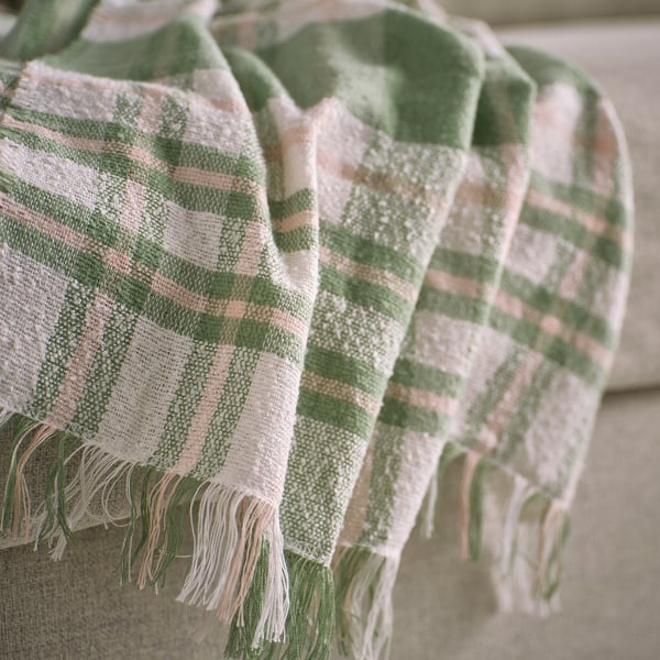 Textured, striped throw blanket with fringe in green and cream resting on a sofa. Soft, lightweight weave visible.