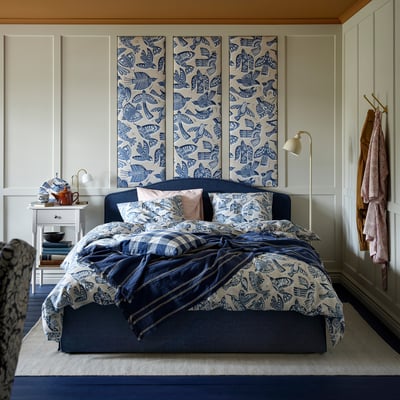 Cozy bedroom with blue BITTERSÖTA bedding; bird print, matches large wall art, complementing nightstands with lamps.