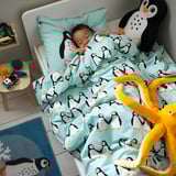 A child sleeps on a penguin-themed bed with blue bedding and a plush penguin pillow.