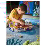 Child plays with blue ship toy on yellow rug. Boy in yellow shirt, sitting on rug with blue ocean design. Ship toy on floor with small red boat.