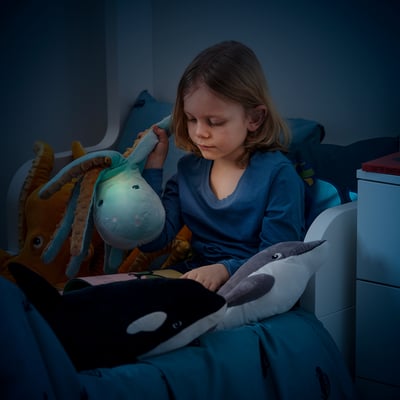 Girl reads in bed with octopus lamp, creating cozy atmosphere.