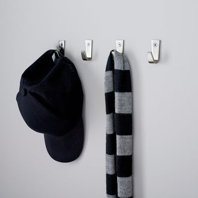 Four metallic wall hooks hold a black cap and a striped scarf, neatly organizing accessories in a hallway.