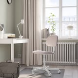 Home office: sleek white desk, chair, lamp, & plant. Curtains & window views. Black bag.