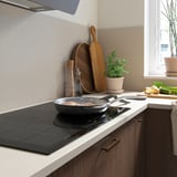 Modern kitchen with sleek black induction cooktop, wooden utensils, plants, and fresh produce on counter.