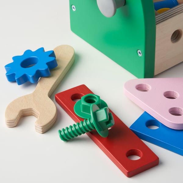 Colorful wooden toy tools, including wrenches, screws, and blocks, alongside a green toolbox, arranged neatly for play or storage.