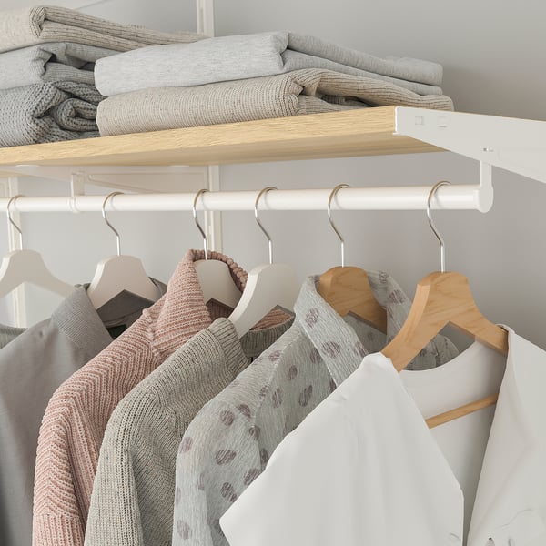 A closet with wooden and white hangers holding clothes like sweaters and a jacket. Folded blankets are stored on a shelf above.