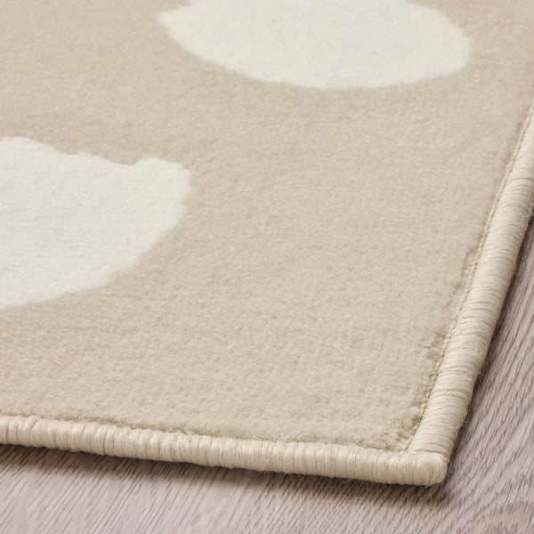 Neutral-tone area rug with subtle dot pattern, made of durable, stain-resistant polypropylene, folded on light wooden floor.