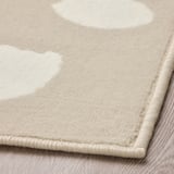 Neutral-tone area rug with subtle dot pattern, made of durable, stain-resistant polypropylene, folded on light wooden floor.