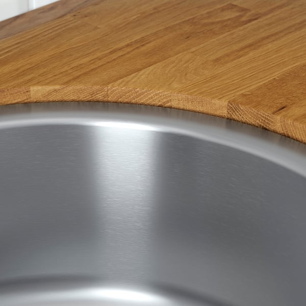 A stainless steel sink with polished, reflective interior and a sleek edge, meeting a wooden countertop.