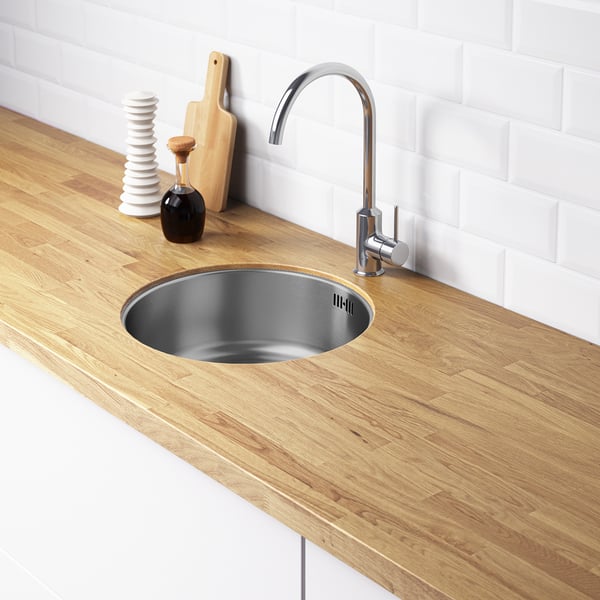 Modern kitchen sink with silver tap on wooden counter, stainless steel sink, decorative items, white backsplash.