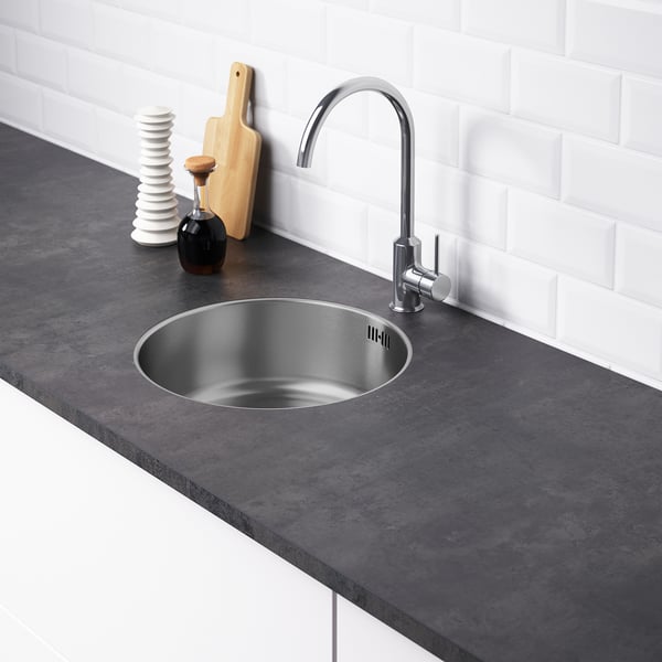 Modern kitchen sink with sleek tap and dark countertop against white tiles.