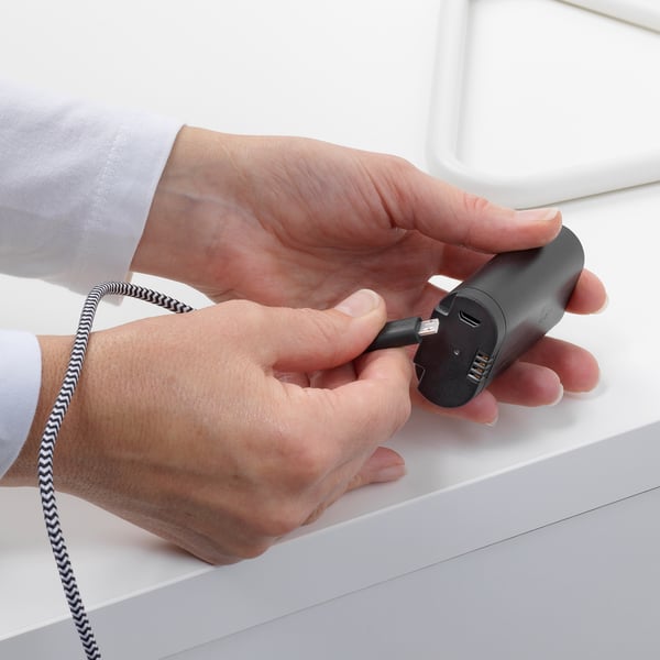 Person holding a BRAUNIT battery pack, attaching a usb cable for charging.