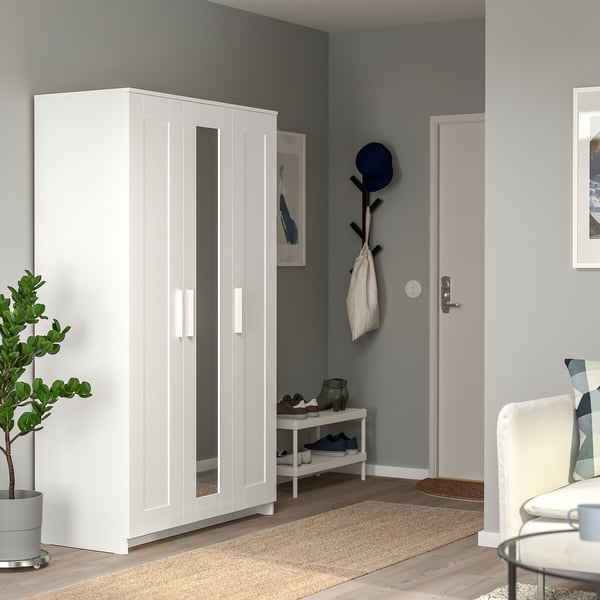 Modern white BRIMNES wardrobe with mirror door beside entrance, sleek design.