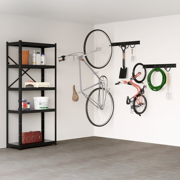 Black BROR shelving unit holds heavy items like tools, bikes. Bikes hang on wall hooks alongside garden tools and hose.