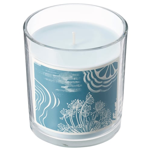A BUKETTAPEL blue scented candle in a clear glass jar. It has a floral design and is cylindrical in shape.