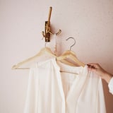 A wooden hanger holds a white blouse on a brass hook, showcasing its non-slip design with grooves.