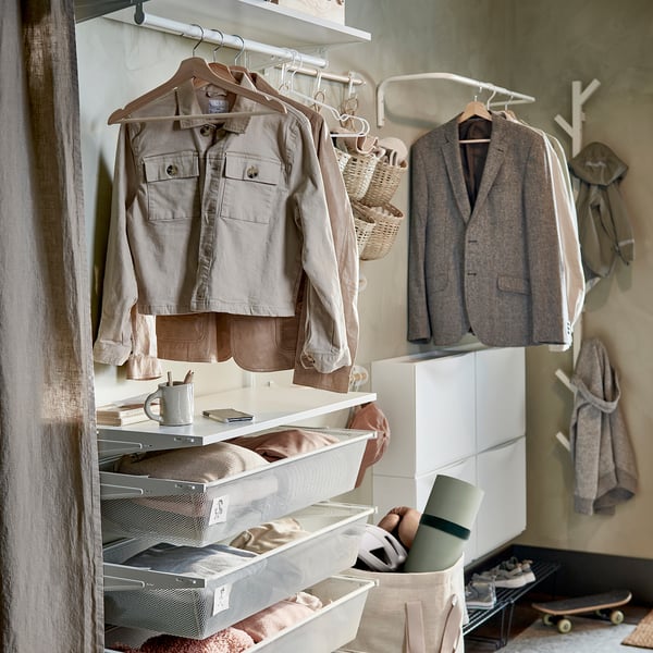 Organized closet with beige BUMERANG hangers made of solid wood, holding jackets and jeans, white mesh drawers and a skateboard.