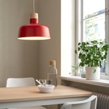Cozy dining area with red BUNKEFLO pendant lamp over light wood table, complemented by minimalist chairs and small decor.