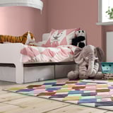 Kids room with BUSENKEL rug, colorful harlequin pattern, soft and durable, fits under bed, surrounded by plush toys, pink walls.