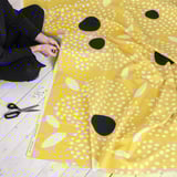 Person working with yellow patterned fabric, scissors, and pins on a table.