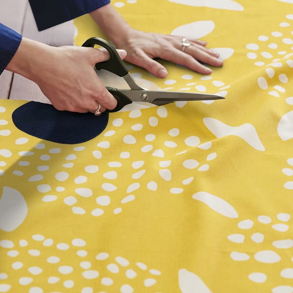 Person cuts yellow patterned fabric with scissors.