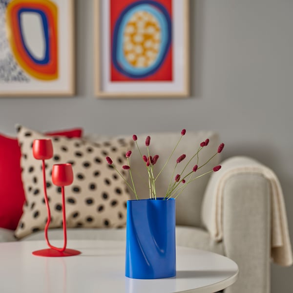 Blue CHILIFRUKT vase with flowers on white table, larger than red candle holder.