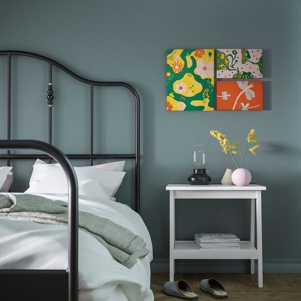 Colorful colorado gran floral print hangs above white side table in calming blue bedroom with metal bed and green bedding.