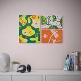 Three colorful wall art pieces with flowers and leaves above white cabinet with plant, headphones, and books.