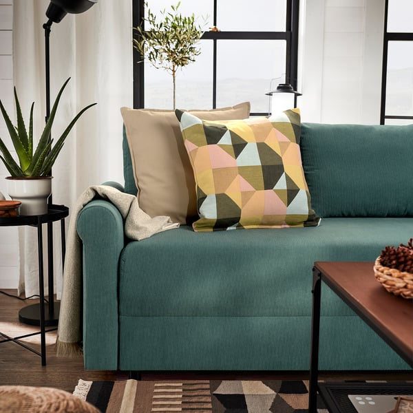Modern living room with teal sofa, colorful pillows, plants, and wooden table.