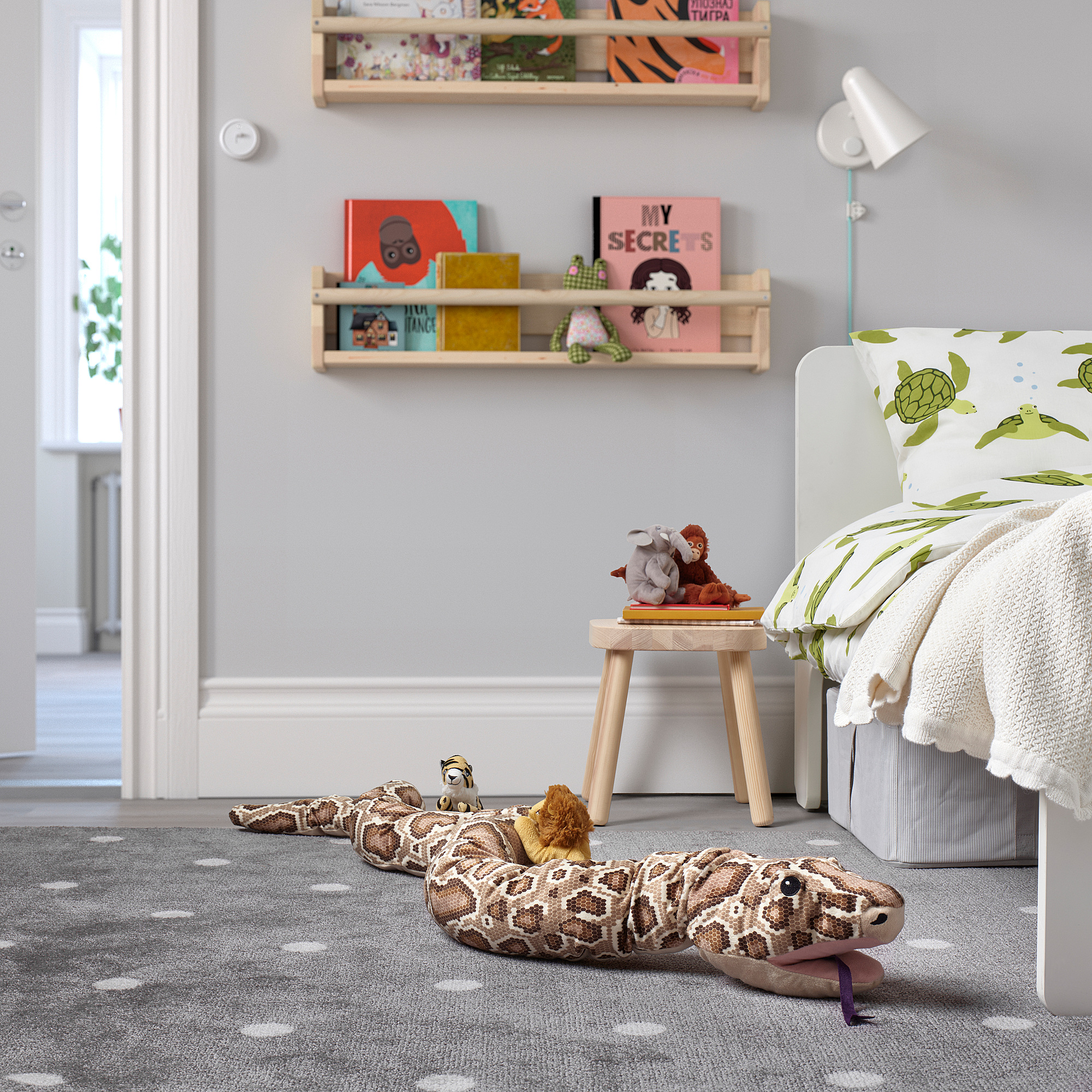 Childs room with tan snake toy, turtle pillow bed, stool, book-filled shelves, grey carpet with white dots.