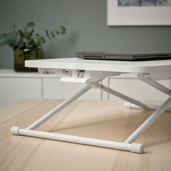A white laptop stand on a wooden desk, holding an open laptop at a raised, ergonomic height for comfortable working.