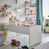 Kids playroom with white DUNDRA table, wooden shelves, colorful toys, and stuffed animals; bright and playful scene.